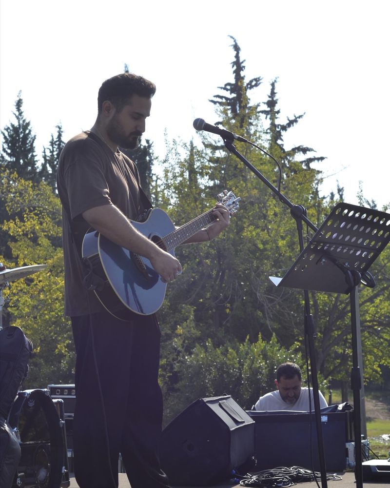Metehan Canpolat mikrofon başında akustik gitar çalıyor
